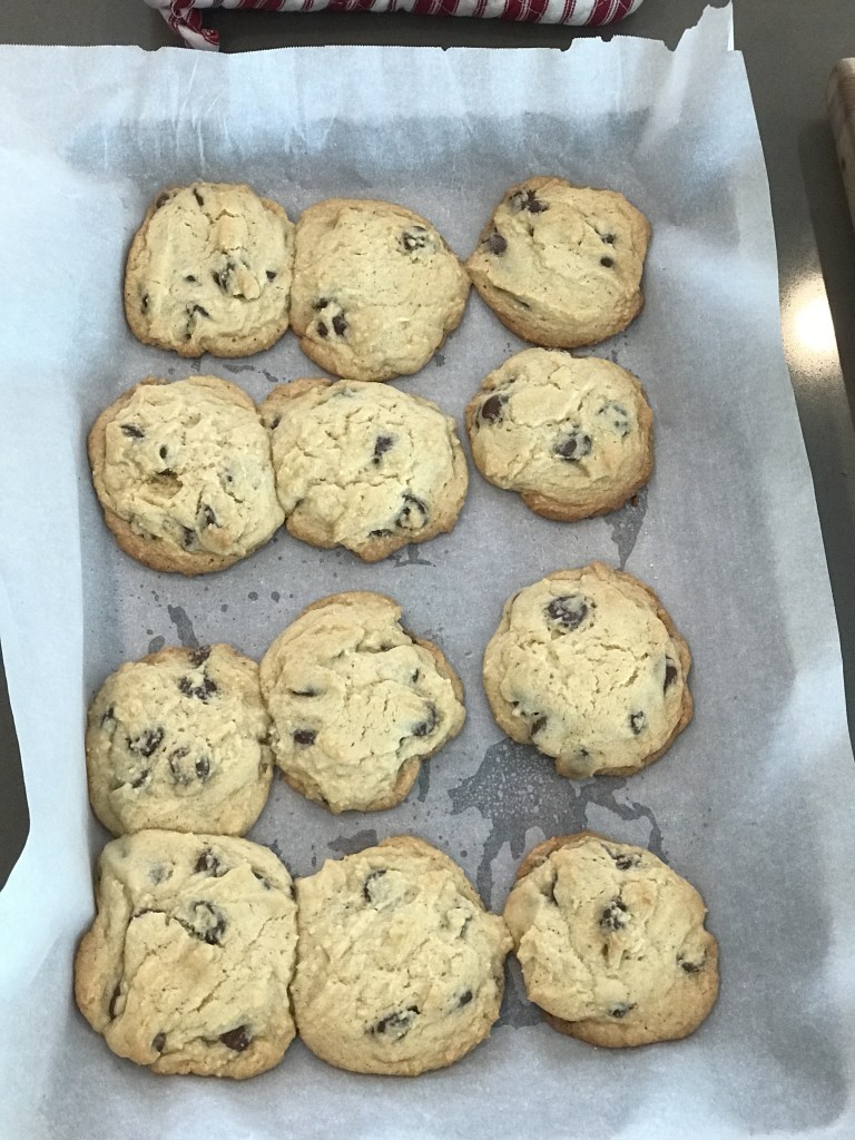 Homemade chocolate chip cookies cooling on a parchment-lined baking sheet.